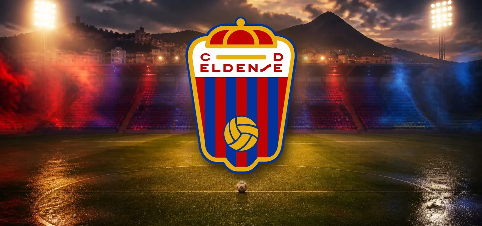 Escudo del CD Eldense sobre el césped iluminado de un estadio al anochecer